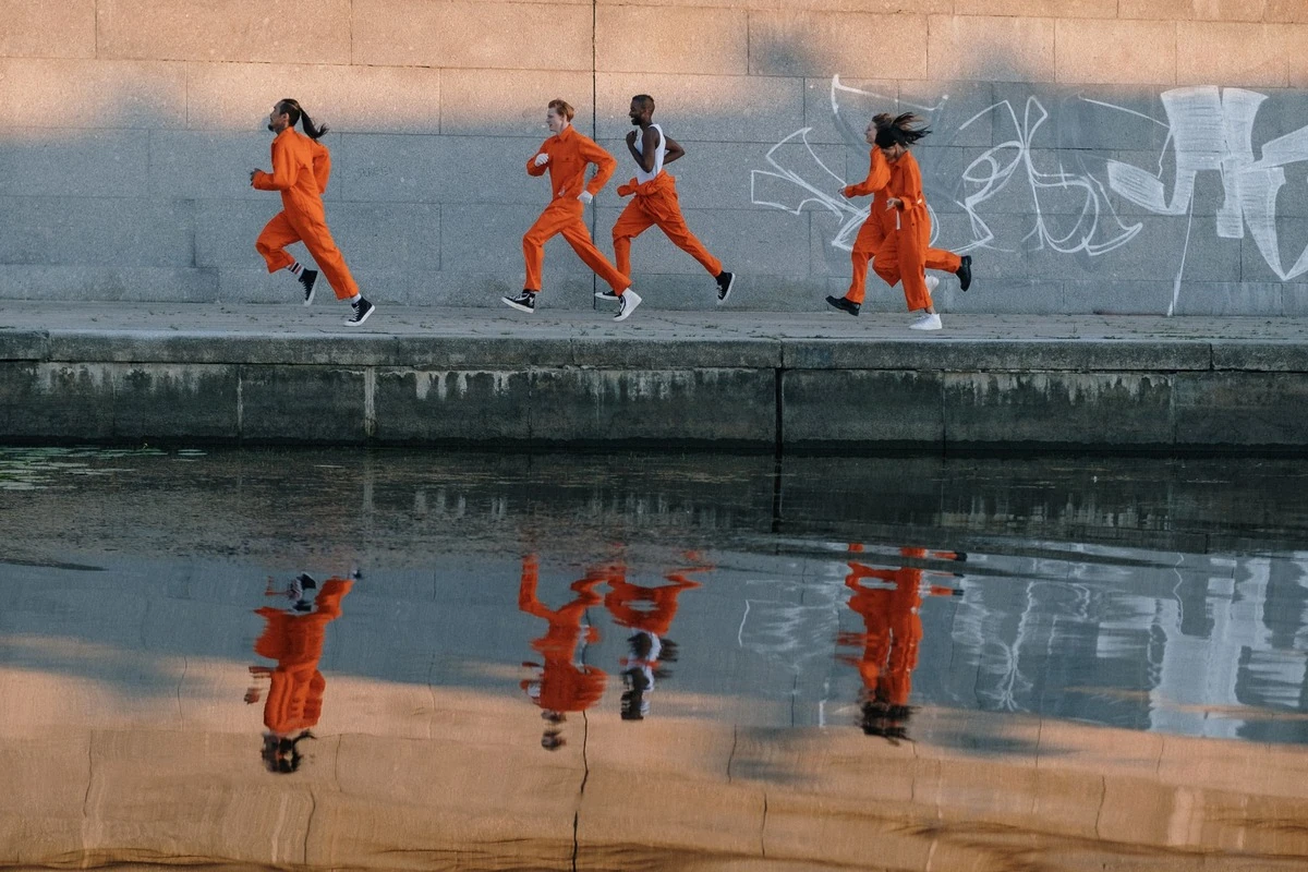 Cinco corredores con ropa naranja junto a un canal, reflejados en el agua