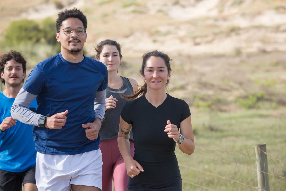 Cuatro personas corriendo juntas por un camino de tierra con vegetación al fondo