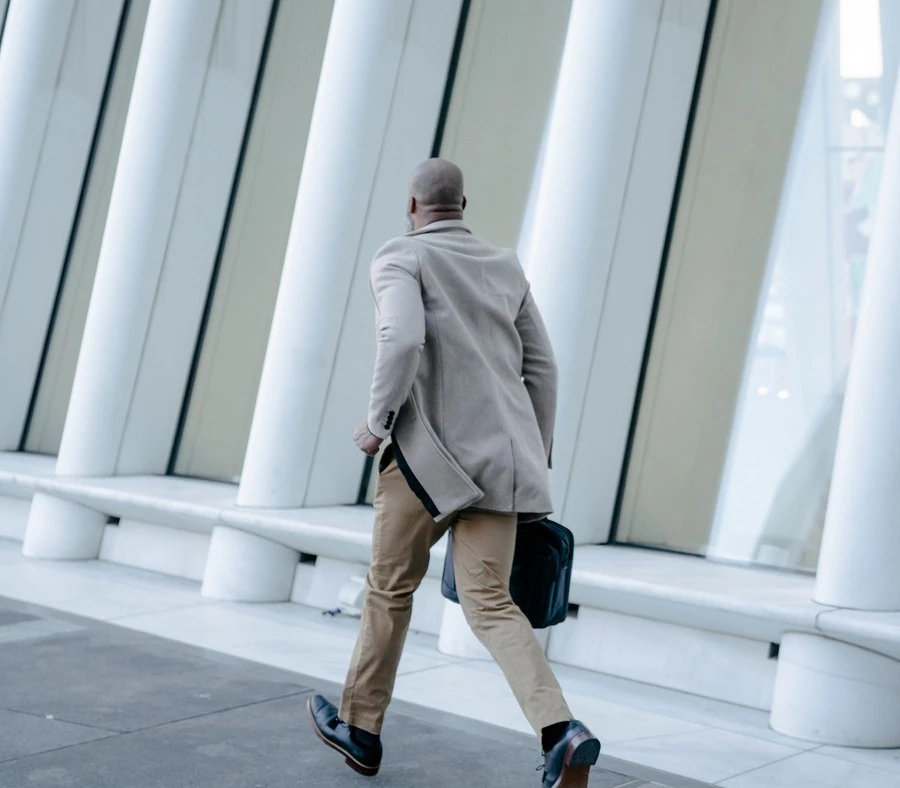 Hombre con traje y maletín caminando a paso rápido junto a una columnata blanca