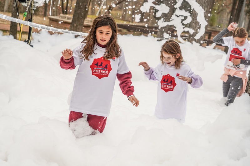 Dos niñas con la camiseta de la carrera corriendo entre espuma blanca.