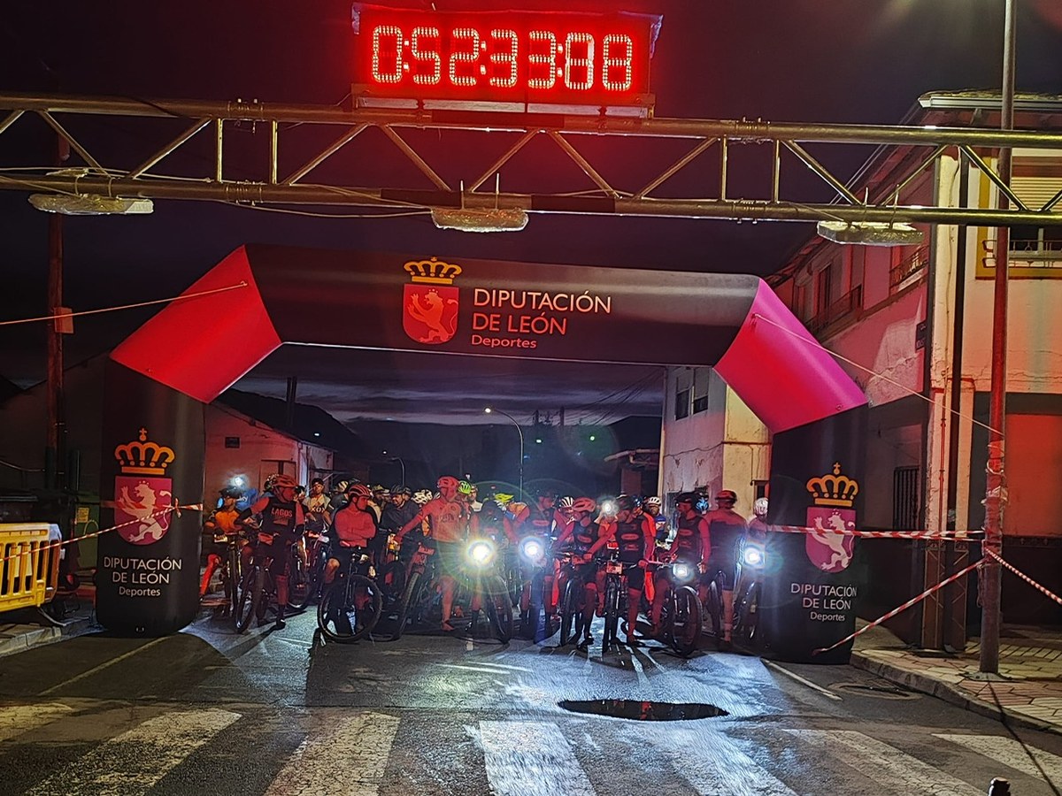 Salida nocturna de ciclistas de montaña con las luces encendidas bajo el arco hinchable de la Diputación de León, con el cronómetro en lo alto