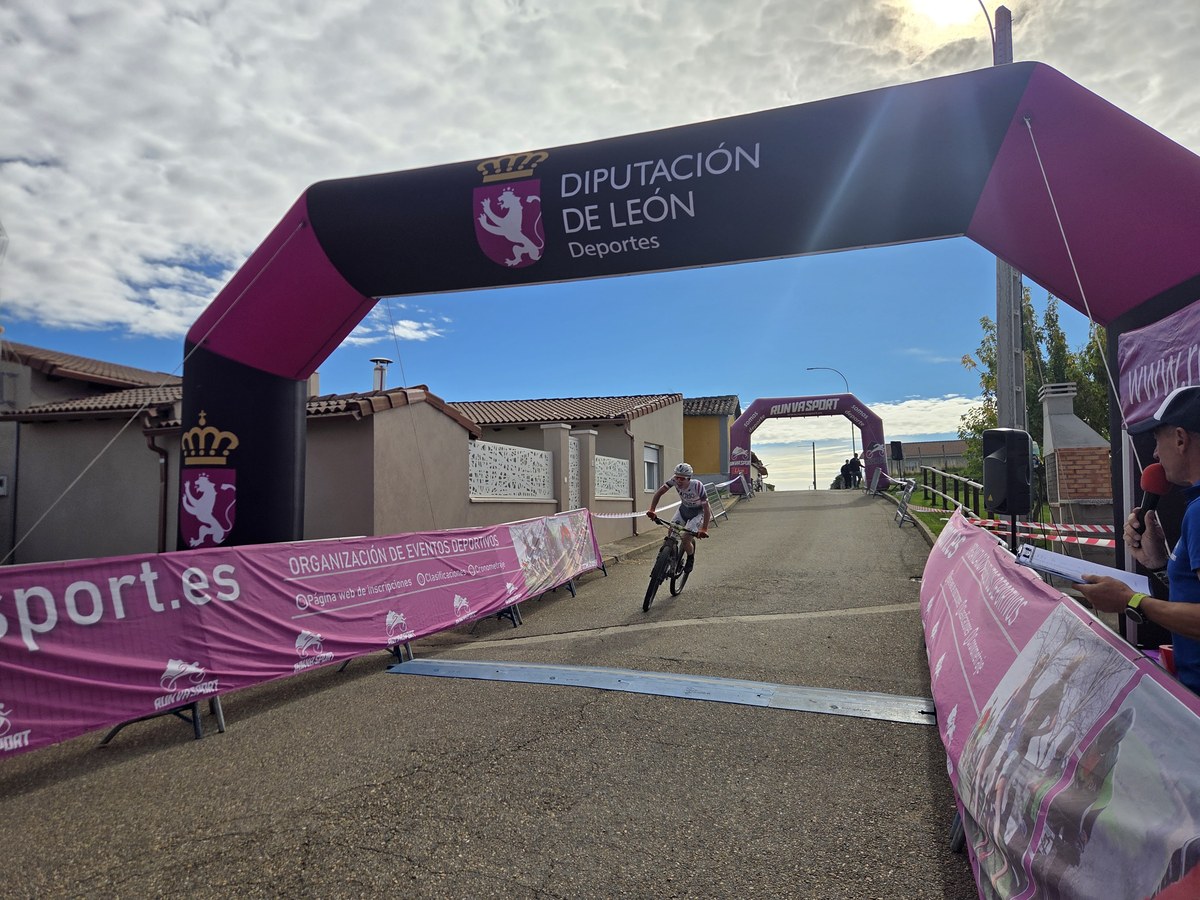 Un ciclista pasa bajo el arco hinchable de la Diputación de León, entre vallas con publicidad rosa