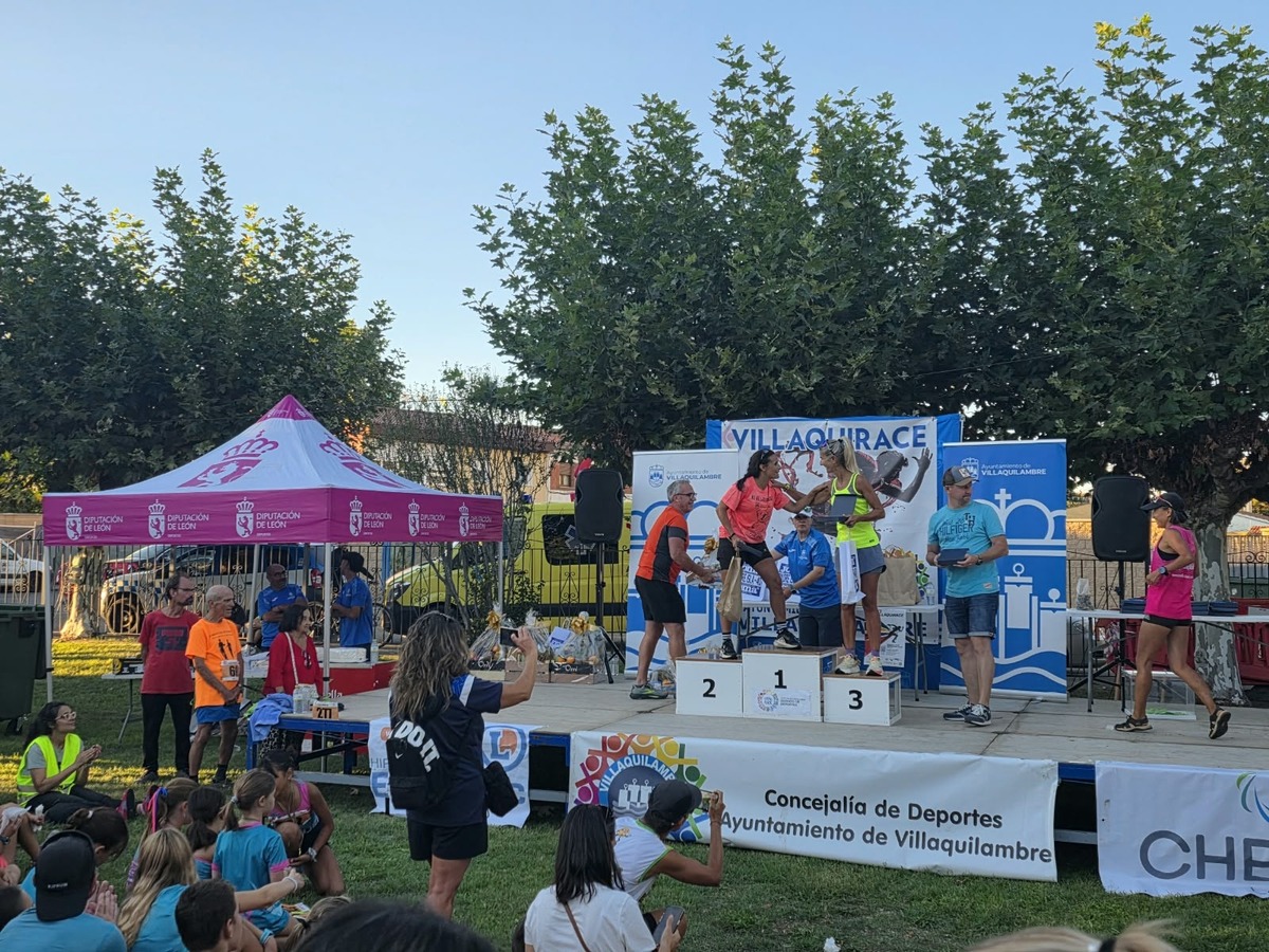 Entrega de premios sobre el podio, con las tres primeras clasificadas en los cajones 1, 2 y 3 y el cartel de la carrera al fondo