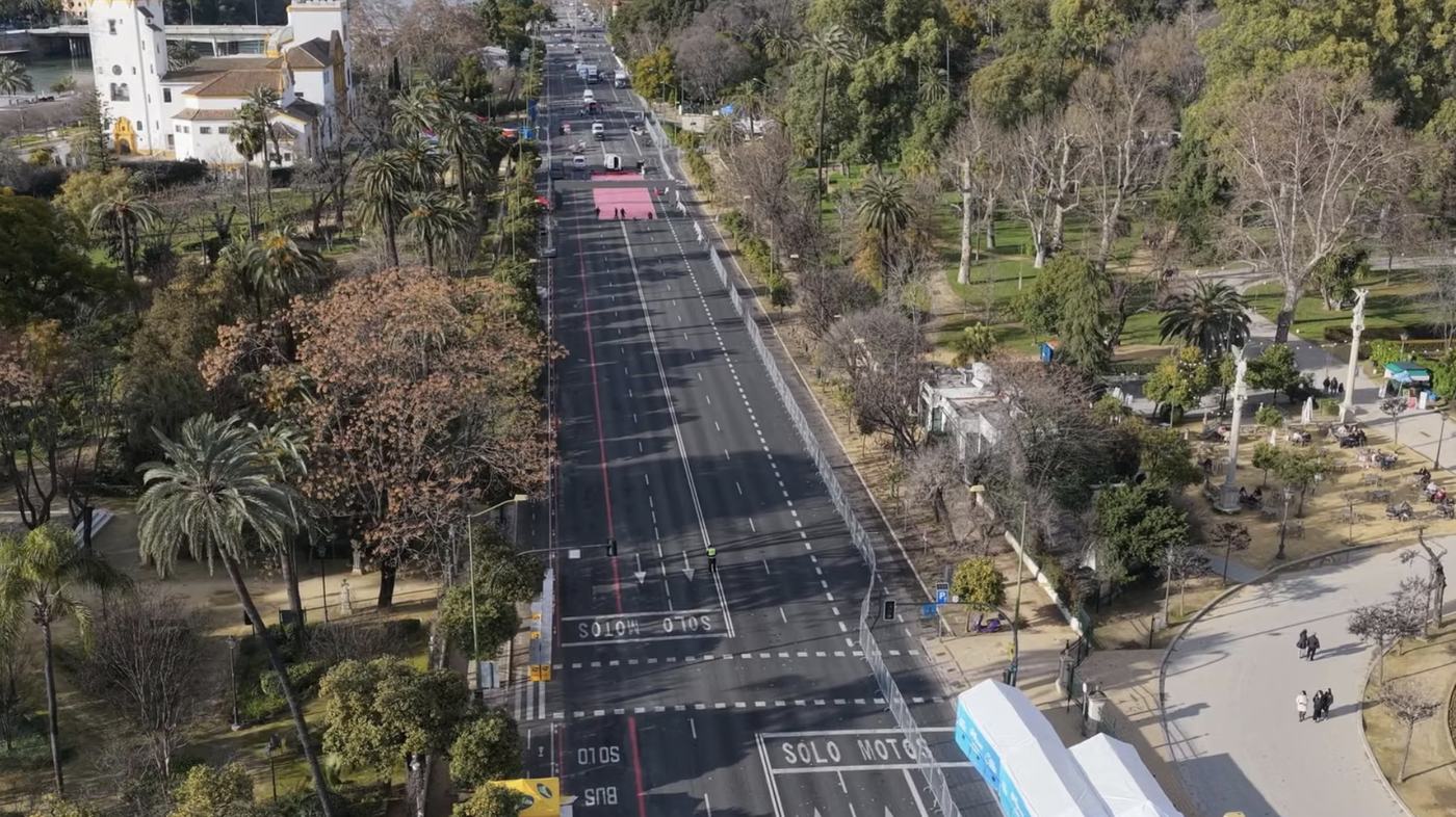 Vista aérea de una avenida de varios carriles cerrada al tráfico, flanqueada por palmeras y jardines, con señalización pintada en el asfalto y carpas blancas montadas junto al paseo lateral